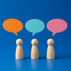Three wooden figures stand beneath vibrant speech bubbles against a blue backdrop, symbolizing collaborative discussions and communication, ideas