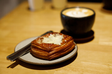 Cup of hot milk latte coffee and Mushroom danish pastry on table.