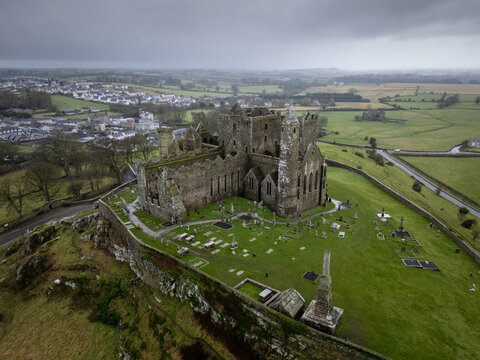 Aerial view of the Rock of Cashel's majestic ruins rising from a verdant hill, a testament to history against the backdrop of a moody, clouded sky, Cashel, County Tipperary, Ireland.