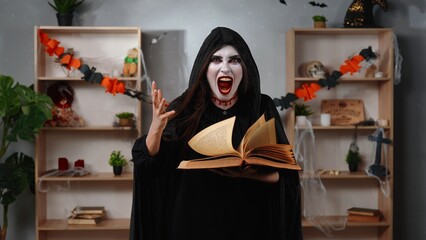 Scary witch woman with an open book in a room decorated for Halloween
