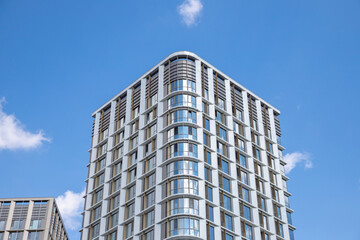 Obraz premium Modern apartment building with glass facade on blue sky in urban landscape during daylight. view from below from street.