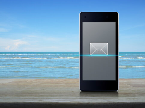 email flat icon on modern smart mobile phone screen on wooden table over blue sky with white clouds, Business communication online concept