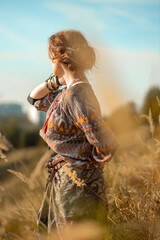 Portrait of a young woman in nature. Beautiful girl in boho style clothes stands in a field of ears of corn. Freedom, love of life