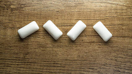 The simple arrangement of white gum pieces on a textured wood surface, ideal for themes of cleanliness and freshness.