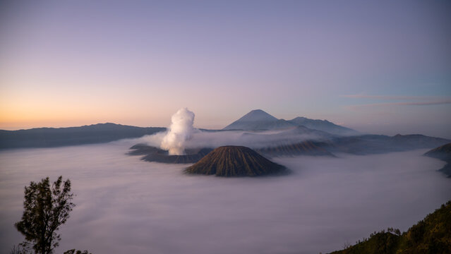 Aerial view of Mount Bromo volcano at sunrise surrounded by clouds and mist in East Java, Indonesia. Scenic volcanic landscape with smoke, mountains, and dramatic sky. - Powered by Adobe