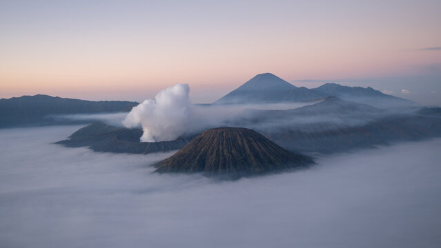 Aerial view of Mount Bromo volcano at sunrise surrounded by clouds and mist in East Java, Indonesia. Scenic volcanic landscape with smoke, mountains, and dramatic sky. - Powered by Adobe