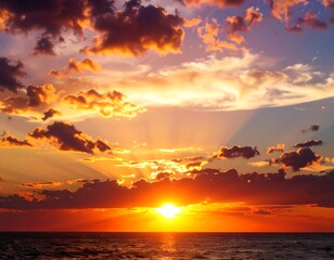 Fototapeta premium A breathtaking sunset paints the sky with vibrant hues of orange, red, and gold, as the sun dips below the horizon, casting dramatic light on the clouds and the tranquil ocean.