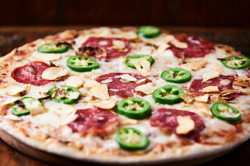 Pizza with salami, mozzarella cheese and jalapeno pepper. Wooden background. Soft focus.	