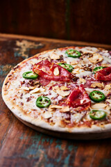 Pizza with salami, mozzarella cheese and jalapeno pepper. Wooden background. Soft focus.	