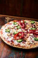 Pizza with salami, mozzarella cheese and jalapeno pepper. Wooden background. Soft focus.	