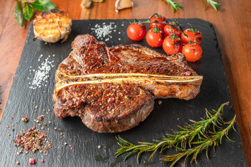 Grilled T-bone steak with seasonings on slate serving plate. Flat lay.