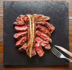 Grilled and sliced T-bone steak with seasonings on slate serving plate. Flat lay.