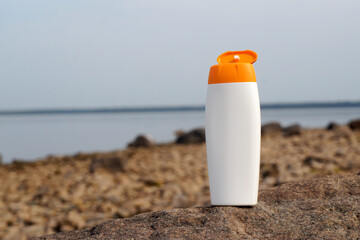 White sunscreen bottle standing on a rock by the lake