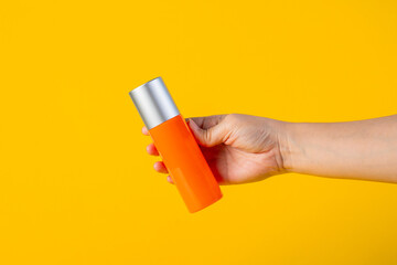 Skin care or sunscreen cosmetic with hand on yellow background.