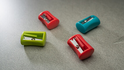 A group of colorful plastic pencil sharpeners, in red, green, and blue, scattered on a simple grey surface.