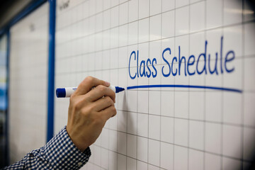 Hand writing Class Schedule on a white grid board with blue marker whiteboard