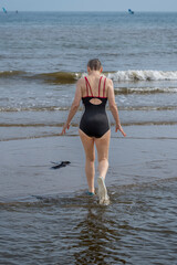 Langrune-Sur-Mer, France - 08 06 2025: A mature woman wearing a blue swimsuit from behind walks in the water to get in the sea