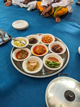 Round platter of traditional Malay saprahan dishes with curries, vegetables, and rice bowls arranged on a blue tablecloth during a wedding feast in Singkawang, Indonesia.