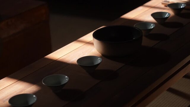 Wooden tea table with traditional tea utensils bathed in slanted sunlight creating soft shadows