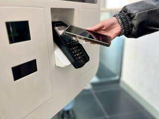Close-up of teenager paying for takeaway food using mobile phone contactless payment at self-service kiosk. Concept: cashless payments, modern technology, digital everyday life.