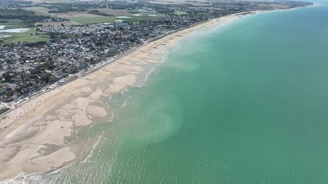 Aerial view of Juno Beach, where the tan sand meets the turquoise water, beside the town, a contrast of natural beauty and human settlement, Berni&egrave;res-sur-Mer, Normandy, France.