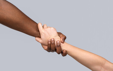 Interracial forearm shake, helping , humanity and brotherhood concept, helping hands, rescue gesture. One caucasian and one african hand. Woman and african woman hand. Helping hand, rescue