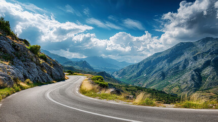 Naklejka premium Majestic mountain road weaving through lush green landscapes under a vibrant sky filled with fluffy clouds