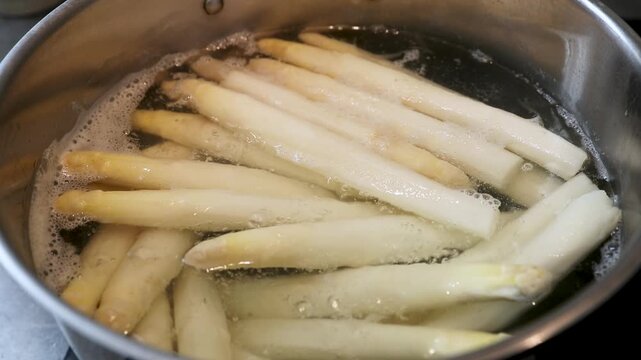 Botte d'asperges blanches fraichement &eacute;pluch&eacute;es en train de cuire dans une casserole d'eau en &eacute;bullition. Sc&egrave;ne culinaire - France.