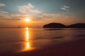 Fototapeta premium Golden sunset casting fiery reflections on the calm sea, with a lone sailboat on the horizon. 