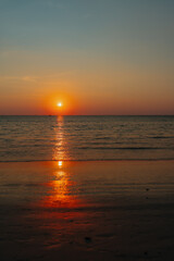 Fototapeta premium Golden sunset casting fiery reflections on the calm sea, with a lone sailboat on the horizon. 