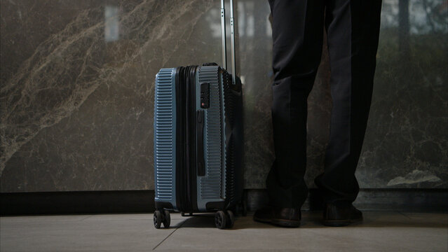 Traveler with suitcase standing at hotel lobby, luggage on wheels ready for check in