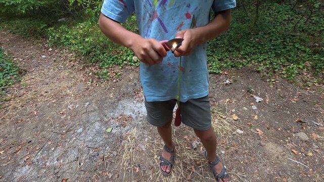 Boy using fire starter to create sparks outdoors in the forest. Close-up of hands striking ferro rod with knife to ignite fire, practicing bushcraft and survival skills