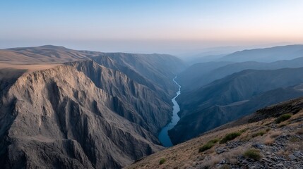 Naklejka premium Deep canyon view; steep cliffs meet a blue river under a hazy sky