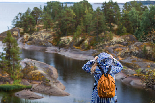 Tourism. Hiking. Ladoga skerries on Lake Ladoga. A female tourist in a raincoat with a backpack on the rocky islands looks into the distance. Republic of Karelia, Russia.