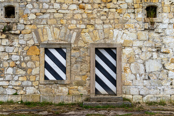 Old stone wall with two black and white striped wooden shutters. Vintage architecture detail