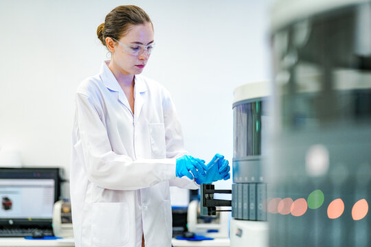 A focused female pathologist assistant carefully loads tissue slides into an automated IHC stainer, ensuring precise preparation for cancer diagnostics and biomedical research in a modern lab.