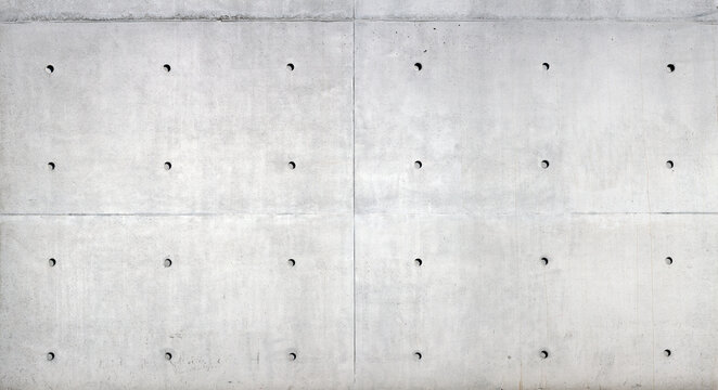 A concrete surface with a distinctly rough, irregular texture. The structure shows porous inclusions, fine cracks, formwork board marks, and irregular shadows due to the grainy surface.