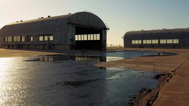 Two large historical aircraft hangars constructed during major global conflict for maritime patrol seaplanes with coastal urban area visible in the distance