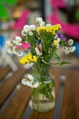 Rustic bouquet of wild flowers in glass bottle with water on wooden table