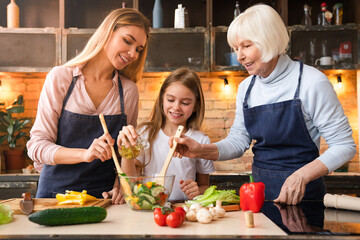 Front view of beautiful little girl that pours oil in salad while young mother and grandmother helping her to mix it. Three generations of women cooking healthy food at home
