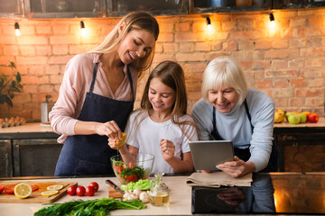 Beautiful young woman squeezing lemon in fresh vegetable salad with her little cute daughter....