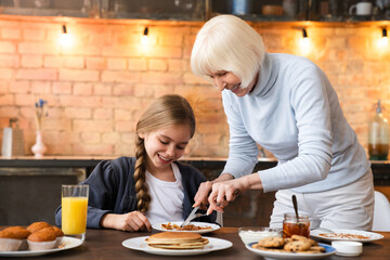 Indoor shot of happy grandmother that helping with breakfast to her granddaughter at the kitchen...