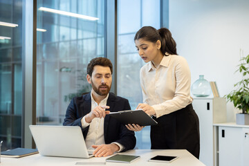 Fototapeta premium Business colleagues discussing a project using laptop and clipboard in office