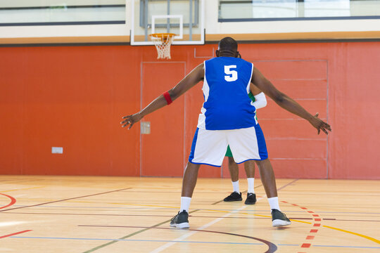 African american mid adult man in blue white jersey 5 guarding opponent on court under hoop