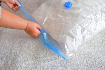 A woman zips a vacuum bag with a blanket. The concept of saving space and carefully storing seasonal items. Compact hermetic bag.
