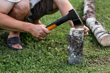 The axe is in the man's hand and is stuck in a birch log. Preparing firewood for the winter season. Logging. Timber, tools for cutting wood.