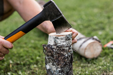 The axe is in the man's hand and is stuck in a birch log. Preparing firewood for the winter season. Logging. Timber, tools for cutting wood.