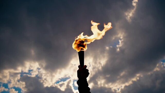 powerful and glorious of silhouetted human hand holding brightly burning flaming torch high over dramatic cloudy sky
