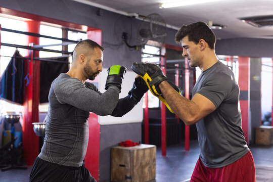 Diverse trainer and trainee punching with green gloves and mitts next to wooden box at boxing gym