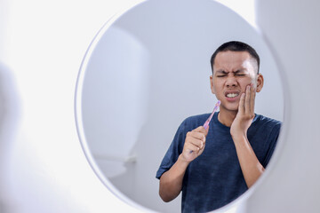 Young Asian Man With Toothbrush Suffering from Toothache in Bathroom